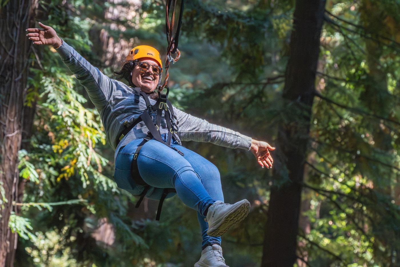 Smiling zipliner in an orange helmet flying through green forest canopy